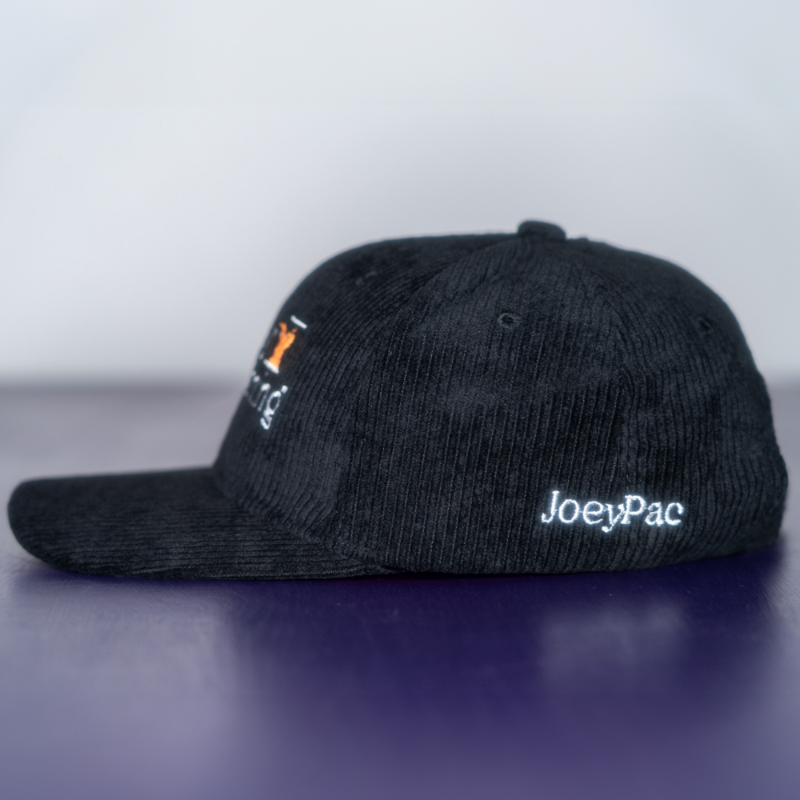 The side of a black corduroy baseball cap with 'JoeyPac' embroidered in white on the lower portion of the hat.