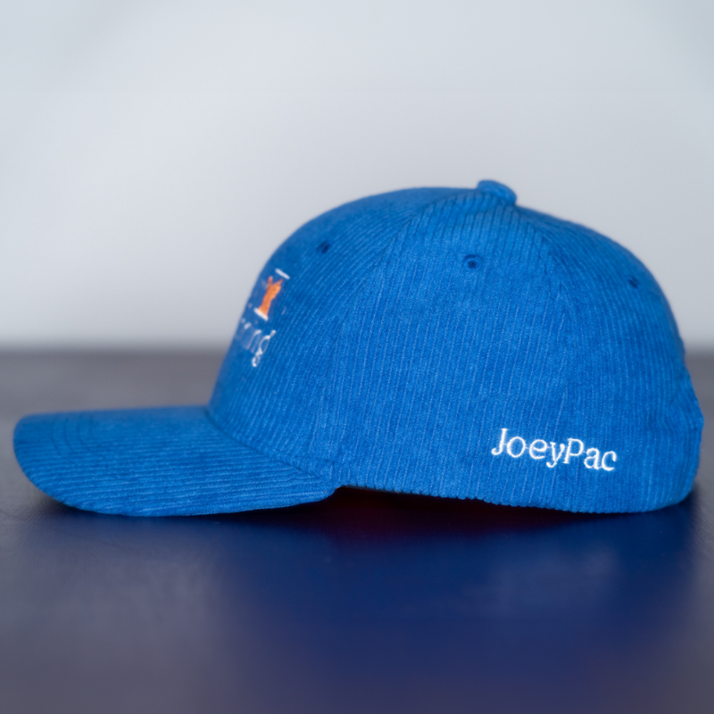 The side of a blue corduroy baseball cap with 'JoeyPac' embroidered in white on the lower portion of the hat.