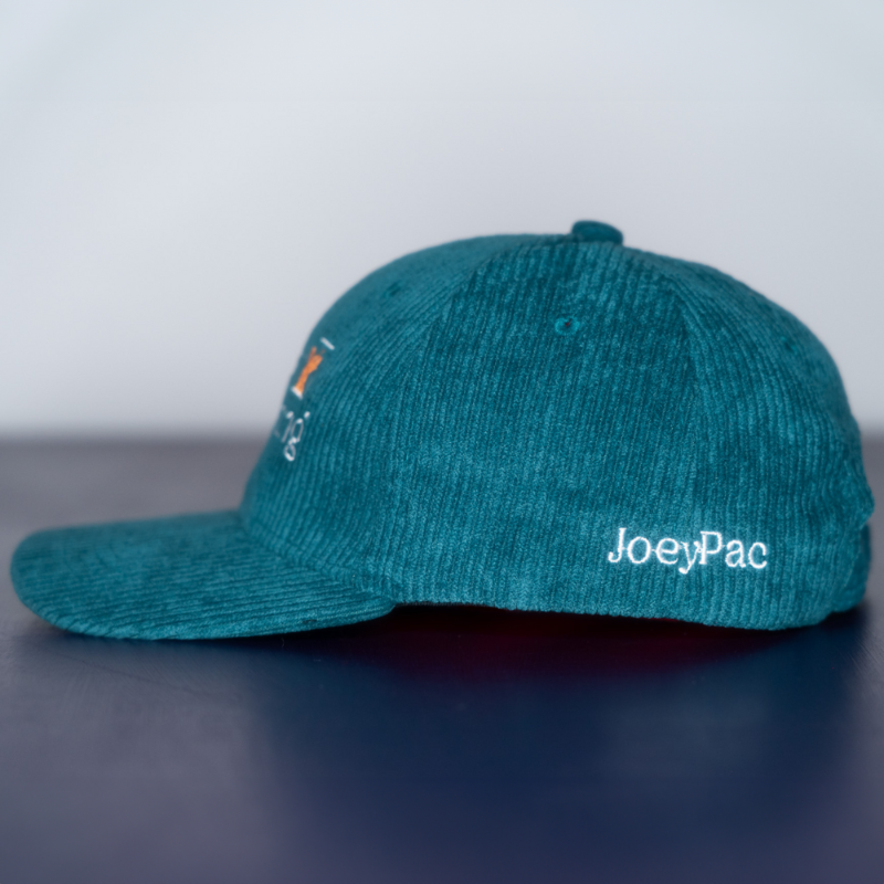Side of a teal corduroy baseball cap with 'JoeyPac' embroidered in white toward the bottom on a reflective surface with a light gray background.