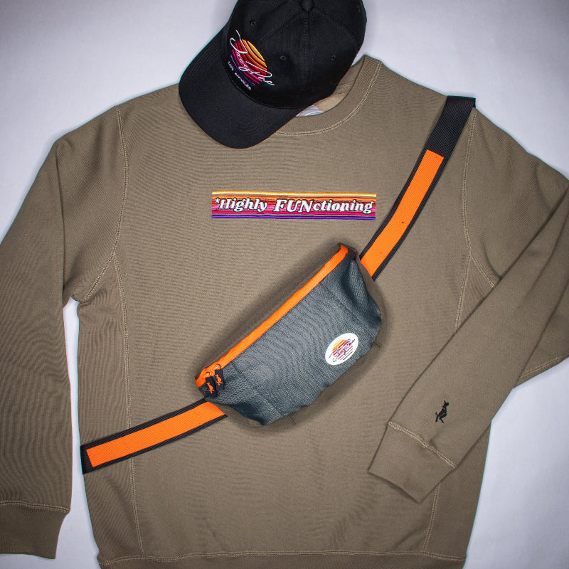 Olive green sweatshirt with a fanny pack and black cap on a white background